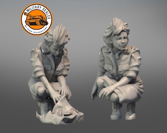 May include: Two gray painted figurines of women in military uniforms. One figurine is kneeling and holding a folded flag. The other figurine is standing with her hands clasped in front of her.