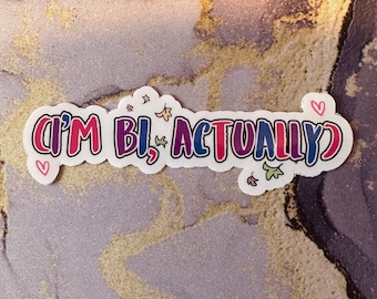 May include: A white sticker with the text "(I'M BI, ACTUALLY)" in pink, purple, blue, and green lettering. The sticker has a white outline and small hearts and leaves around the text.
