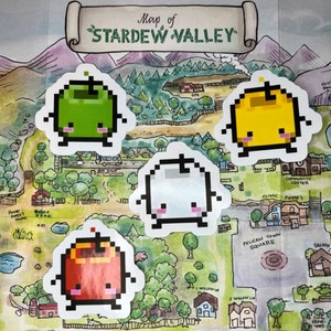 May include: A selection of pixelated fruit stickers in green, yellow, white, and red, each with a friendly face. They are placed on a map of Stardew Valley, a watercolour illustration showing various locations.