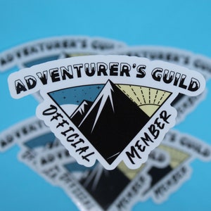 May include: White sticker with a black mountain range and a yellow sun. The text "Adventurer's Guild" is at the top of the sticker, and "Official Member" is on the sides of the sticker.