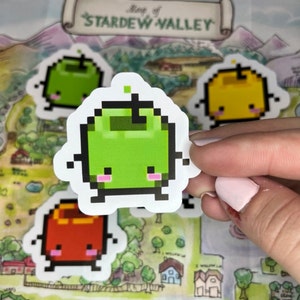 May include: A selection of pixelated fruit stickers, featuring green, yellow, and red apples, each with a cute face. The stickers are shown on a map titled "Map of Stardew Valley."