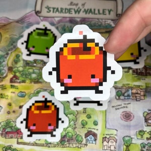 May include: Pixelated stickers of fruit characters, including a red apple with a yellow top, and a green apple. The stickers are on a map of Stardew Valley. The map has the text "Map of Stardew Valley" at the top.