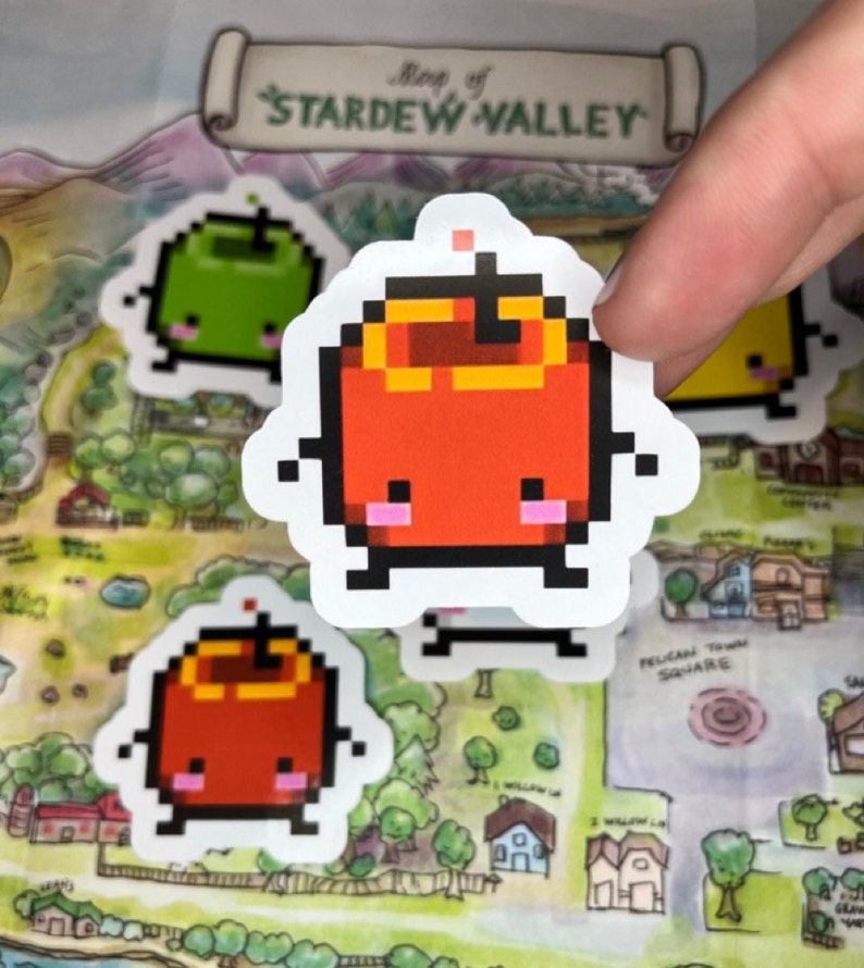 May include: Pixelated stickers of fruit characters, including a red apple with a yellow top, and a green apple. The stickers are on a map of Stardew Valley. The map has the text "Map of Stardew Valley" at the top.