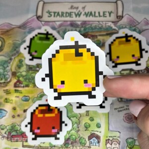 May include: A selection of pixelated fruit stickers, featuring green, yellow, and red apples, each with a cute face. The stickers are placed on a map of Stardew Valley. The text "Map of Stardew Valley" is visible.