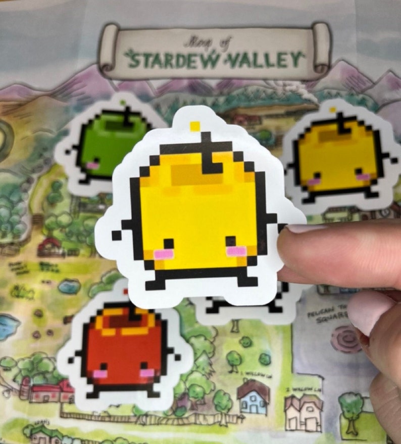 May include: A selection of pixelated fruit stickers, featuring green, yellow, and red apples, each with a cute face. The stickers are placed on a map of Stardew Valley. The text "Map of Stardew Valley" is visible.