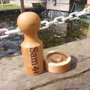 May include: A personalised wooden planter with the name "Sam" engraved on the side. The planter has a round base and a cylindrical top. The planter is made of light brown wood and has a natural finish.