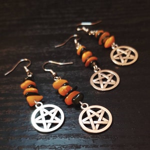 Puede incluir: Tres pares de pendientes con cuentas de piedras preciosas negras y naranjas y dijes de pentagrama de plata.