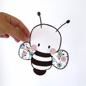 Può includere: Un'ape di cartone animato in bianco e nero con pois colorati sulle ali. L'ape ha un corpo a strisce e un viso carino.