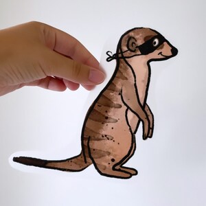 Op de afbeelding: Een bruine en zwarte cartoon-suricate met een zwart oogmasker. De suricate staat op zijn achterpoten met zijn voorpoten omhoog. De suricate heeft een witte achtergrond.