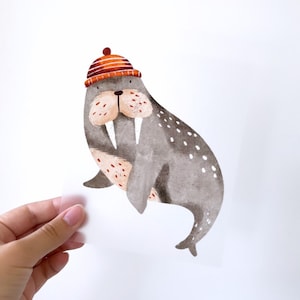 Könnte beinhalten: Eine Aquarell-Illustration eines Walrosses, das einen rot-orange gestreiften Hut trägt. Das Walross ist grau mit weißen Flecken und hat große Stoßzähne.