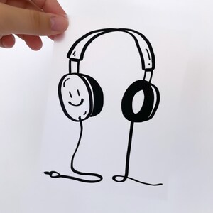 May include: Black and white line drawing of a pair of headphones with a smiling face on one earcup.