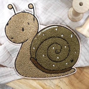 Könnte beinhalten: Eine braune gestickte Schnecke mit einer grünen Schale und weißen Punkten. Die Schnecke befindet sich auf einer hellbraunen Holzoberfläche.