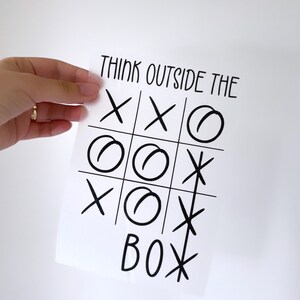 Könnte beinhalten: Ein weißes Blatt Papier mit dem Text "Think outside the box" in Schwarz. Ein Tic-Tac-Toe-Spiel ist mit Kreisen und Kreuzen auf dem Papier gezeichnet.