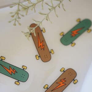 Peut inclure: Quatre autocollants de skateboard colorés avec un motif d'éclair. Les autocollants sont sur un fond blanc.