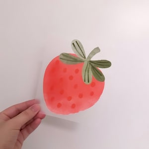 Peut inclure: Une peinture à l'aquarelle d'une fraise rouge avec des feuilles vertes. La fraise est peinte dans un style réaliste avec un fond rose clair.