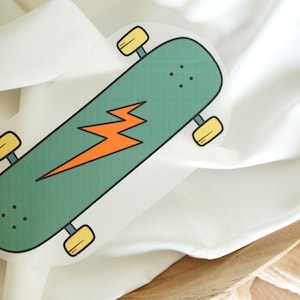Peut inclure: Une planche à roulettes verte avec un graphique d'éclair jaune. La planche à roulettes est sur un fond de tissu blanc.
