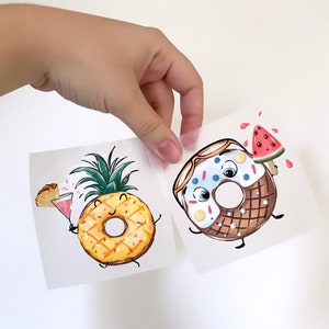 Könnte beinhalten: Zwei illustrierte Aufkleber mit einem Ananas und einem Donut. Die Ananas trägt eine Sonnenbrille und hält ein rosa Getränk. Der Donut trägt eine Sonnenbrille und hält ein Stück Wassermelone. Beide Aufkleber haben einen weißen Hintergrund.