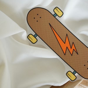Peut inclure: Une planche à roulettes marron avec un graphique d'éclair jaune. La planche à roulettes a des roues jaunes et est sur une surface blanche.