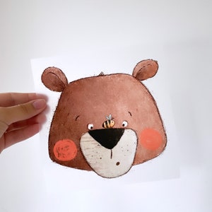 Peut inclure: Un ours brun avec une expression surprise, une petite abeille sur le nez et des joues rouges. L'ours est dessiné dans un style cartoon avec un effet aquarelle.
