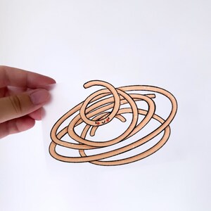 May include: A cartoon illustration of a smiling, light brown spaghetti noodle with a black outline. The noodle is coiled and has a small, smiling face. The image is held by a hand against a white background.