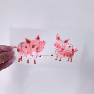 Könnte beinhalten: Zwei rosa Schweine mit schwarzen Flecken tragen Lichterketten in Rot und Weiß. Die Schweine schauen sich an und lächeln.