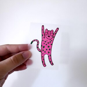 Könnte beinhalten: Ein rosa-grüner Leoparden-Sticker mit einem Cartoon-Leoparden, der seine Arme in die Luft streckt. Der Leopard hat einen glücklichen Gesichtsausdruck.