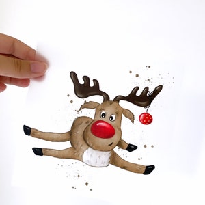 Könnte beinhalten: Ein Cartoon-Rentier mit braunem Fell, schwarzen Geweih und einer roten Nase springt in der Luft. Das Rentier hält einen roten Weihnachtsbaumschmuck mit einer goldenen Schnur.