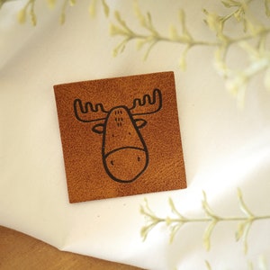 May include: A brown leather patch with a black outline of a moose head.