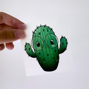 Könnte beinhalten: Ein grüner Cartoon-Kaktus mit runden Brillen und einem lächelnden Gesicht.