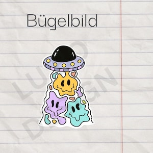 Op de afbeelding: Een kleurrijke strijkapplicatie met een cartoon UFO. De UFO heeft een zwarte koepel en een paarse en gele ring. Daaronder drie lachende gezichten in geel, paars en turquoise. Het woord "Bügelbild" staat bovenaan.