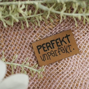 May include: A brown leather tag with black text that reads "PERFEKT unperfekt."