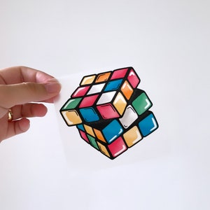 May include: A colourful 3D Rubik's Cube with black outlines. The cube is made up of small squares in red, orange, yellow, green, blue, and white.