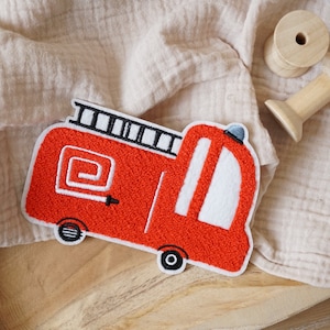 Può includere: Applique di camion dei pompieri in feltro rosso con dettagli bianchi. Il camion ha una scala sul tetto, una manichetta e ruote.