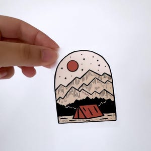 Könnte beinhalten: Eine Schwarzweißillustration einer Bergkette mit einer roten Sonne und Sternen am Himmel. Ein rotes Zelt befindet sich im Vordergrund.