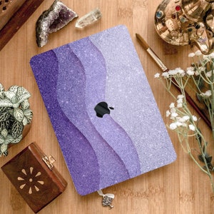May include: A purple and white glitter laptop skin with a wavy design. The skin has a gradient effect, starting with a dark purple at the bottom and fading to a light white at the top. The skin is designed to fit a standard laptop.