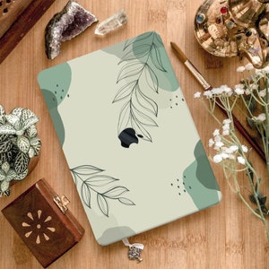 May include: A laptop skin with a green and white abstract design featuring a stylized leaf pattern. The design has a light green background with darker green abstract shapes and a black outline of leaves.