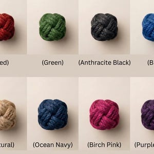 Op de afbeelding: Een verzameling van acht decoratieve touwknopen in verschillende kleuren, waaronder rood, groen, zwart, blauw, naturel, marine, roze en paars. Elke knoop wordt getoond tegen een neutrale achtergrond, met kleurnamen eronder.