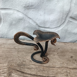 Puede incluir: Un portavelas de metal negro y cobre con forma de hongo y un diseño decorativo de espiral.