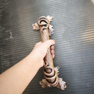 May include: A decorative bronze-colored door handle with a unique design. The handle features a textured, cylindrical grip with a coiled snake motif and leaf accents. The handle is designed to be mounted on a door.