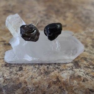 May include: Two black gemstone earrings on a white crystal base.