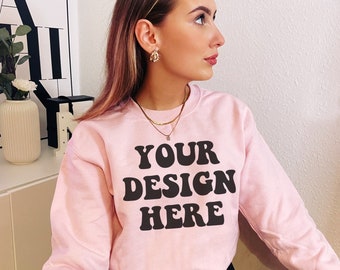 May include: A pink sweatshirt with the text "YOUR DESIGN HERE" in black retro-style lettering.