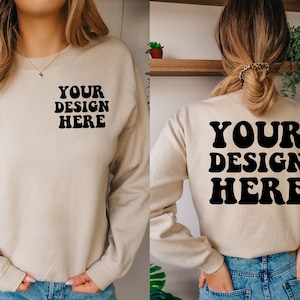 May include: A beige sweatshirt with long sleeves and a crew neck. The front of the sweatshirt has the text "YOUR DESIGN HERE" in black. The back of the sweatshirt has the same text in a larger font.