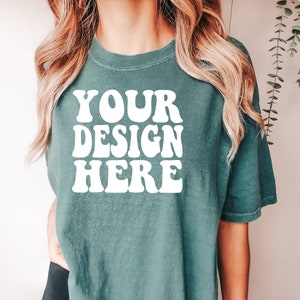May include: A teal blue t-shirt with the text "YOUR DESIGN HERE" in white retro-style lettering.