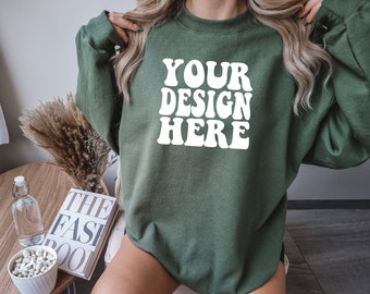 Op de afbeelding: Een groen sweatshirt met de tekst "YOUR DESIGN HERE" in witte letters. Het sweatshirt heeft een losse pasvorm en een ronde hals.