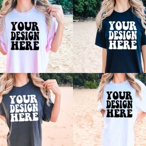 May include: Four different color t-shirts with the text "YOUR DESIGN HERE" printed in black on the front. The shirts are shown on models in a beach setting.