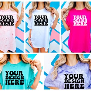 May include: Five different t-shirts with the text "YOUR DESIGN HERE" printed in black on the front. The shirts are in various colors, including pink, white, turquoise, and purple.