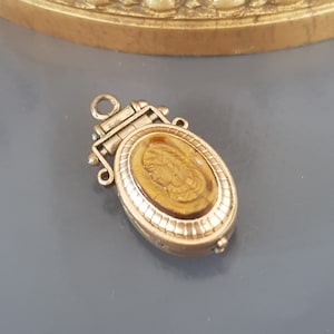 Peut inclure: Un médaillon doré avec une fermeture à charnière et un camée ovale brun avec un motif sculpté.