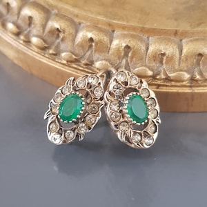 Puede incluir: Un par de pendientes de plata con piedras ovaladas verdes rodeadas de brillantes transparentes.