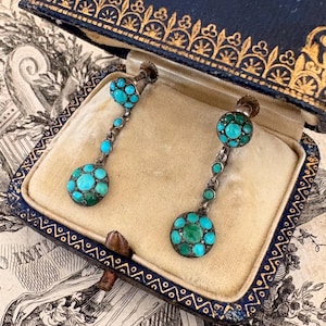 May include: A pair of silver drop earrings featuring circular clusters of small, round turquoise stones. Each earring consists of a top cluster connected by a short chain to a larger bottom cluster, all set in silver with screw-back mechanisms.