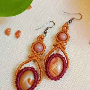 Op de afbeelding: Een paar oranje en mahoniekleurige macramé oorbellen met roze en witte agaatstenen.